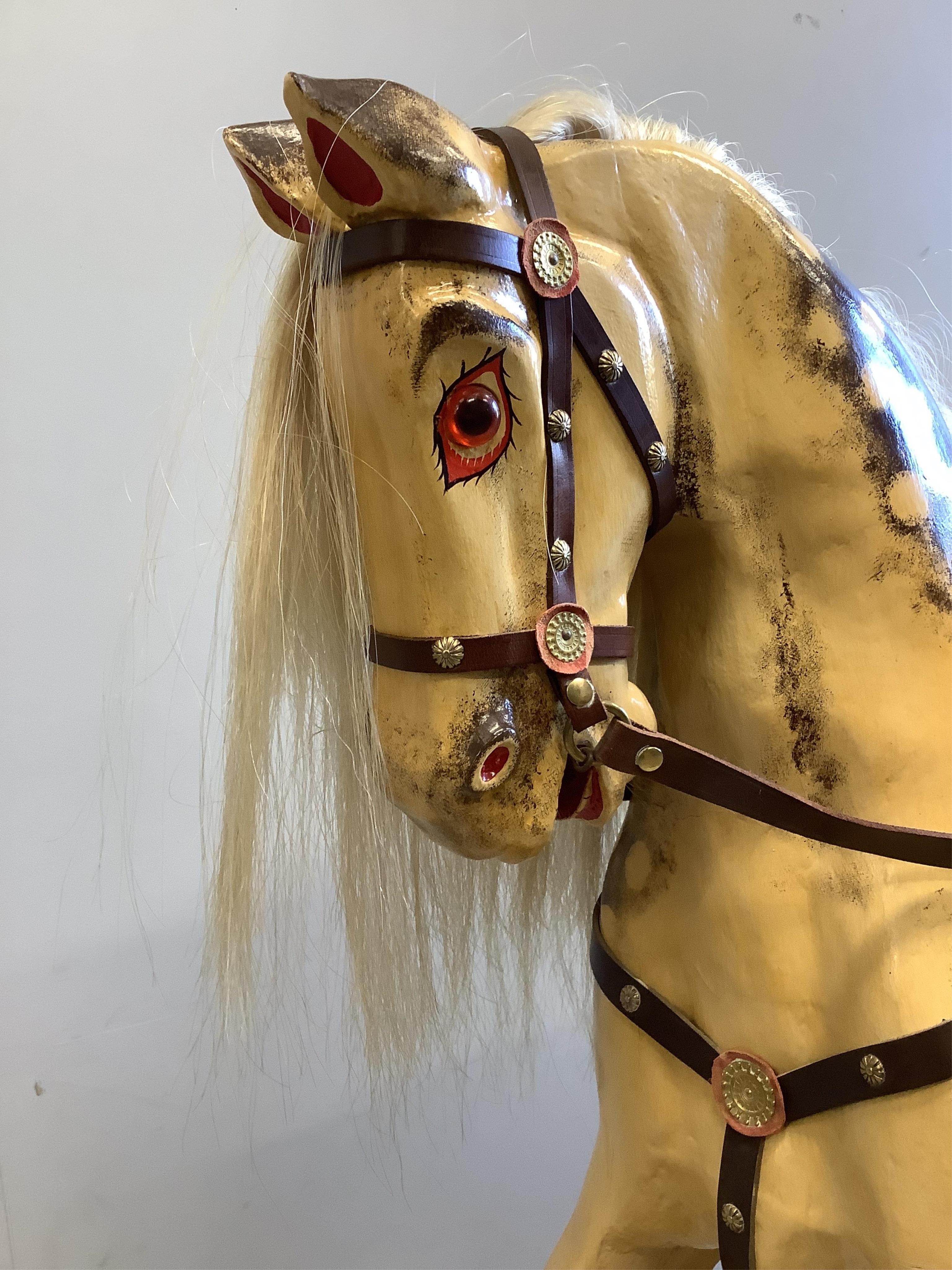 A large carved wooden rocking horse on a pine stand, the body painted in dapple grey, with glass eyes and upholstered leather saddle, height to the top of the head 130cm, length of base 152cm. Condition - fair to good.